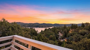 A scenic view from a balcony overlooking a lake, surrounded by dense forest and hills.