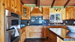 A kitchen with wooden cabinets, a stainless steel oven, and a granite countertop. - Golden Hour Lodge by Avantstay BBQ + Great Room + Multiple Decks Lake & Sunset Views (Lake Arrowhead)