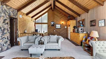 A cozy living room with a stone wall, a fireplace, a dining area, and a kitchen with wooden cabinets.