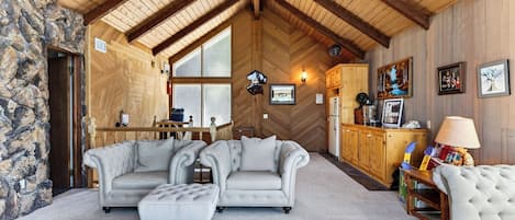 A cozy living room with a stone wall, a fireplace, a dining area, and a kitchen with wooden cabinets.