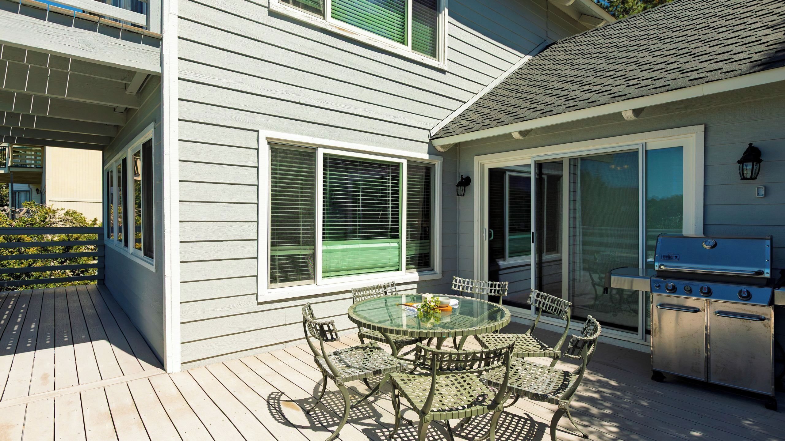 A patio with a glass table and chairs, a grill, and a sliding glass door.