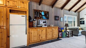 A kitchen with wooden cabinets, a refrigerator, and a dining area with a table and chairs. - Golden Hour Lodge by Avantstay BBQ + Great Room + Multiple Decks Lake & Sunset Views (Lake Arrowhead)