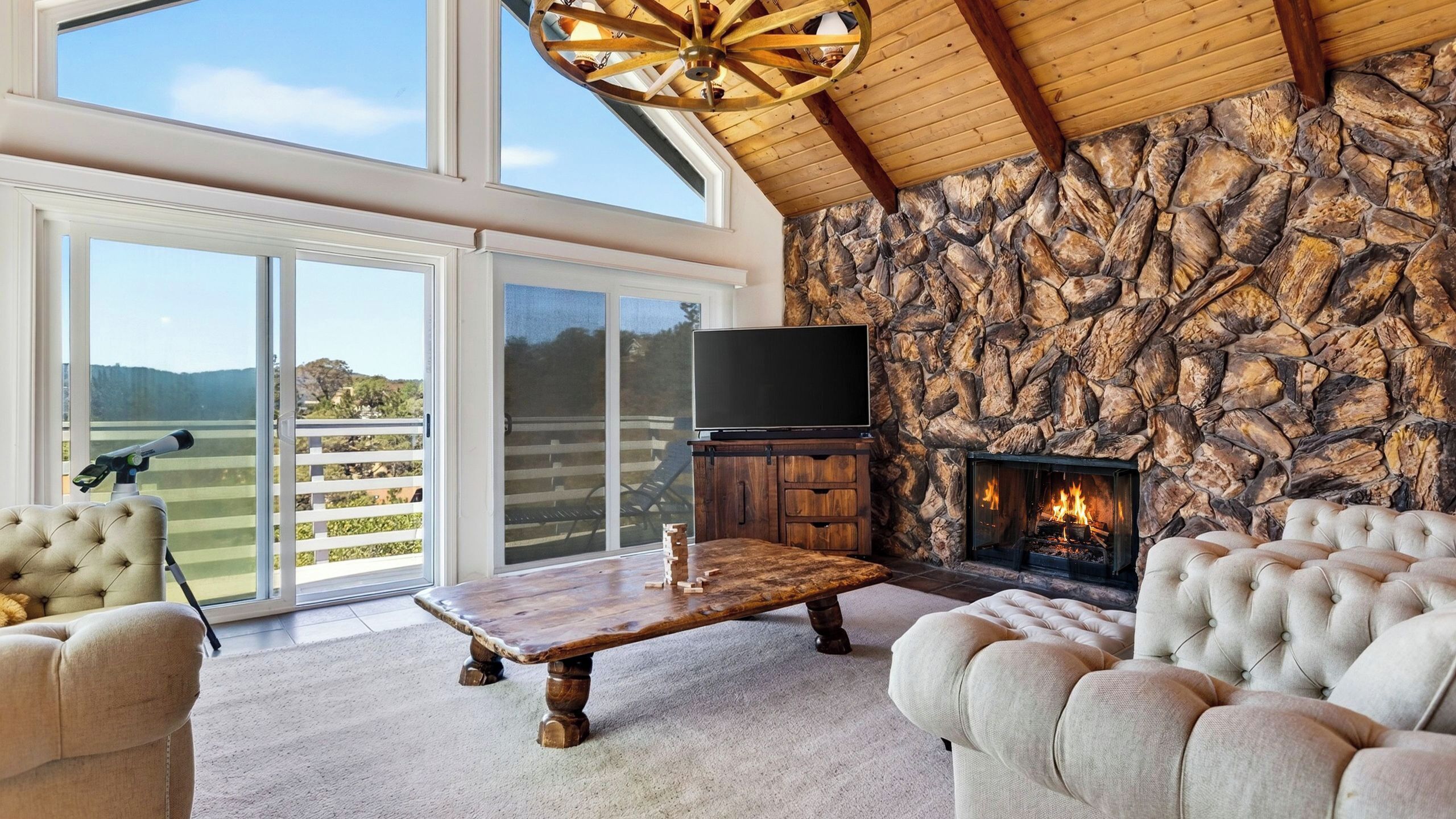 A spacious living room with a stone fireplace, a large flat-screen TV, and a view of the outdoors through large sliding glass doors.