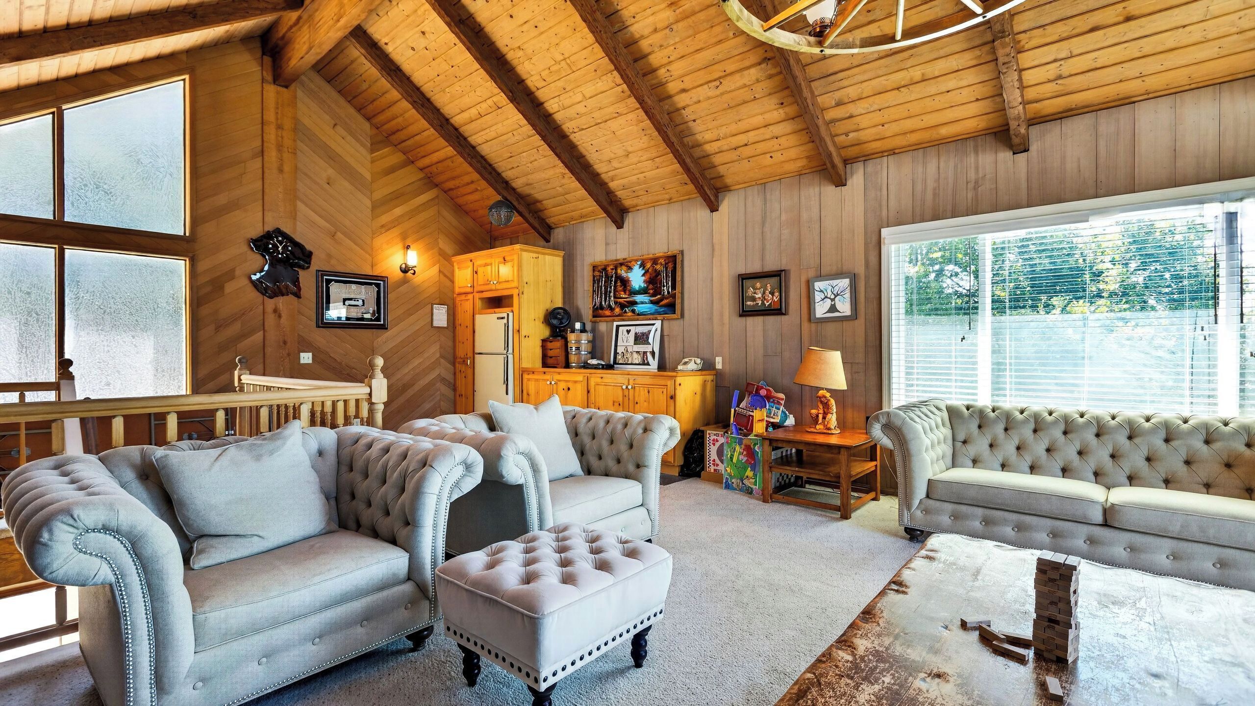 A spacious living room with a high ceiling, wooden beams, and a large window. There are two sofas, a coffee table, and a fireplace.