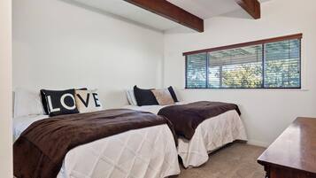 A bedroom with two beds, a window with blinds, and a wooden ceiling beam.