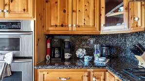 A kitchen with wooden cabinets, a stainless steel refrigerator, a coffee maker, and a kettle. - Golden Hour Lodge by Avantstay BBQ + Great Room + Multiple Decks Lake & Sunset Views (Lake Arrowhead)