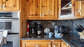 A kitchen with wooden cabinets, a stainless steel refrigerator, a coffee maker, and a kettle. - Golden Hour Lodge by Avantstay BBQ + Great Room + Multiple Decks Lake & Sunset Views (Lake Arrowhead)