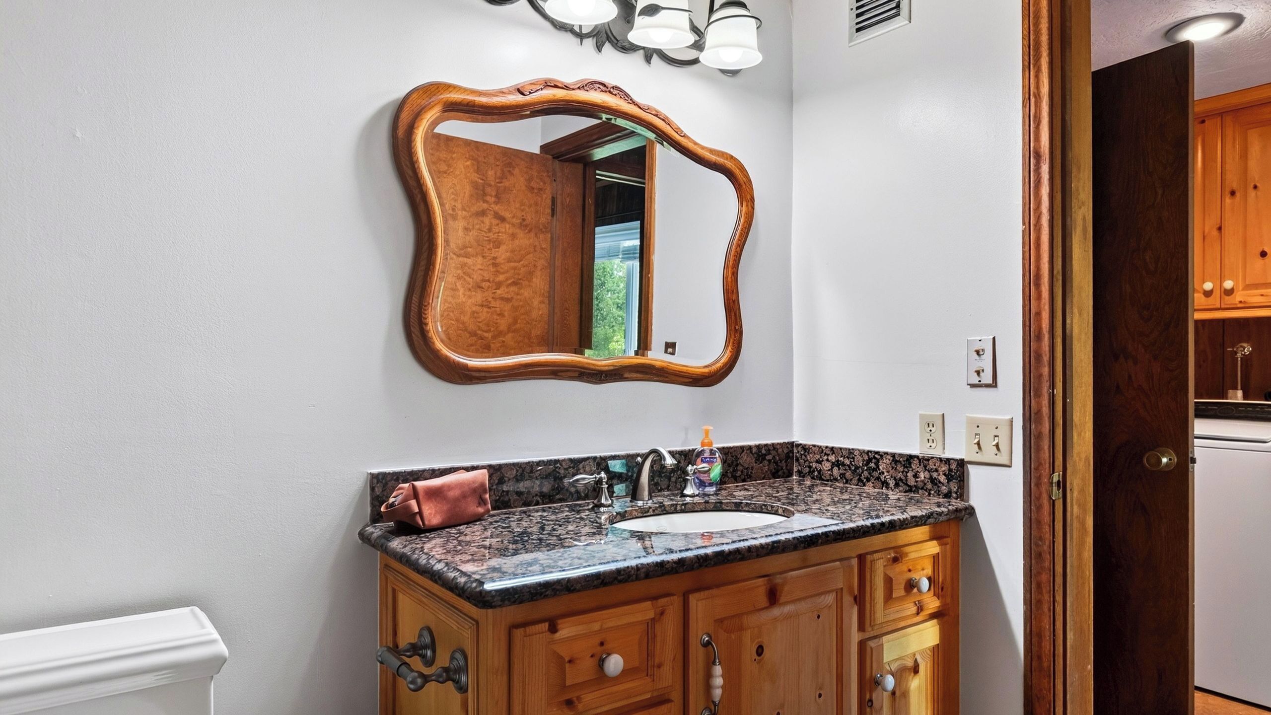 Un bagno con un mobile lavabo in legno, un lavandino e uno specchio con cornice decorata.