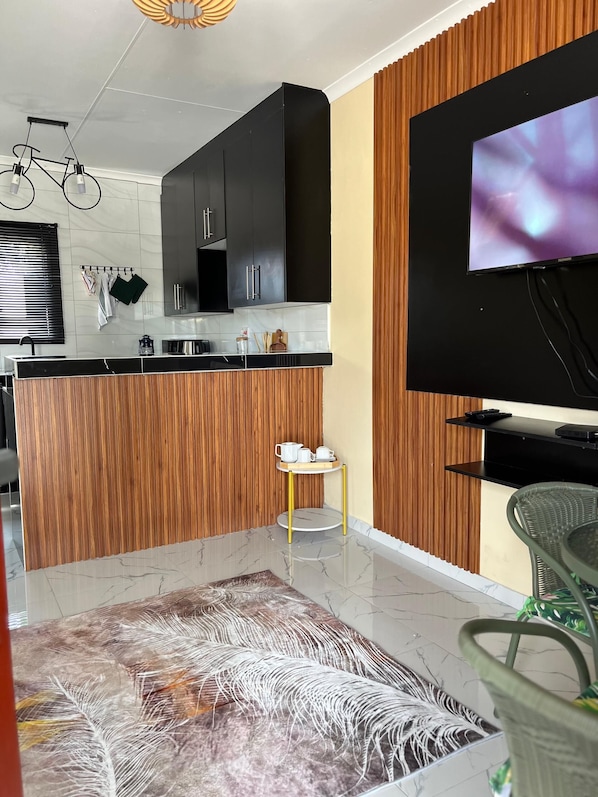 A modern kitchen with black cabinets, a wooden accent wall, a round dining table, and a flat-screen TV mounted on the wall.