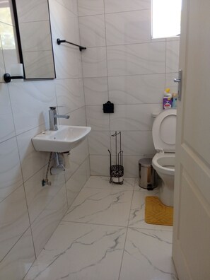 Un baño con lavamanos blanco, inodoro y un cubo de basura.