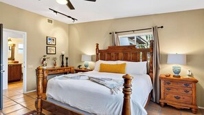 Quarto com cama de dossel, mesa de cabeceira, cômoda e janela com cortinas.