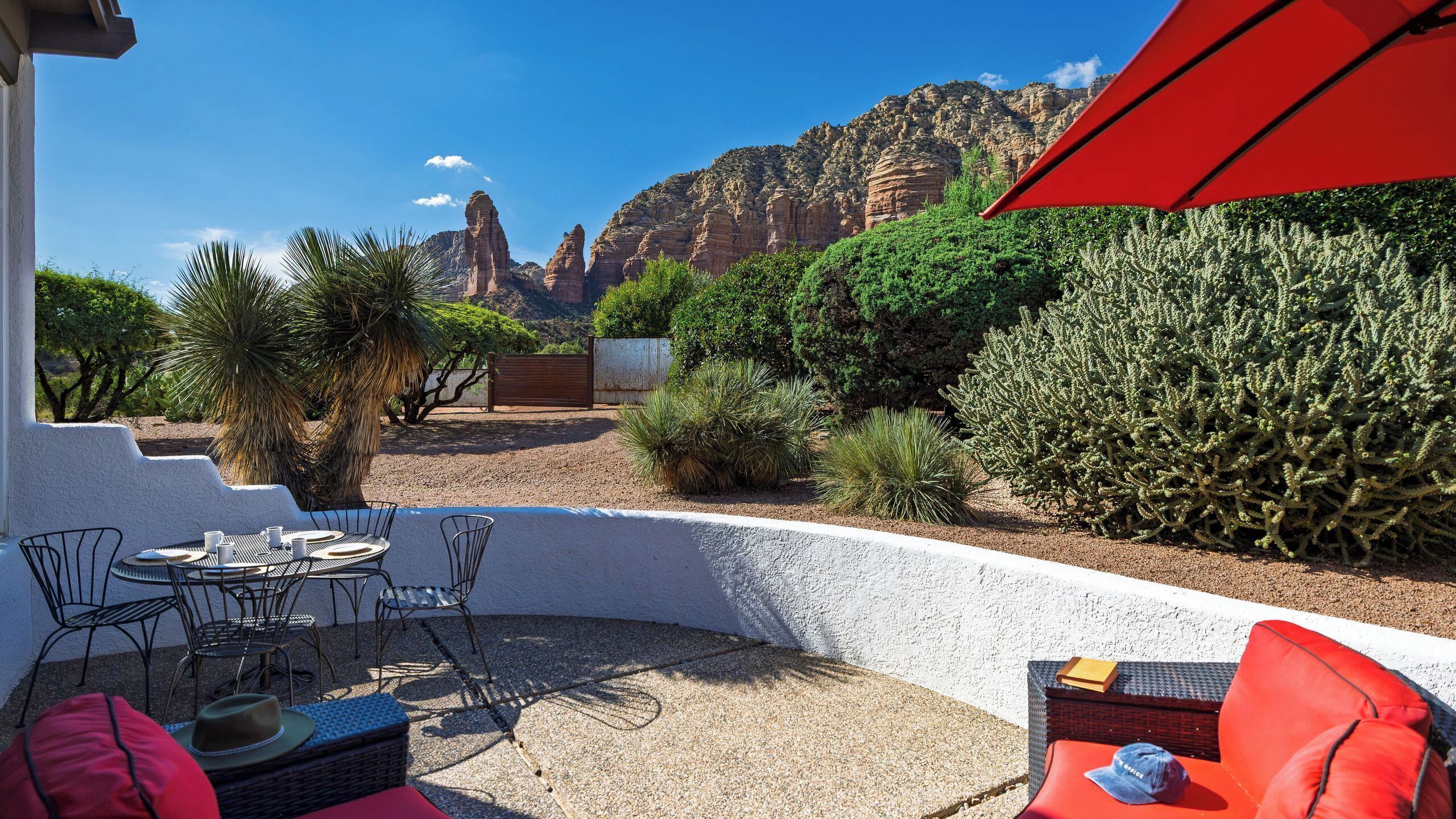 Un patio al aire libre con una mesa y sillas, rodeado de vegetación desértica y vistas de formaciones rocosas.