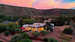 Une maison moderne dotée d’un vaste patio, entourée d’une végétation luxuriante et offrant une vue sur un paysage montagneux.