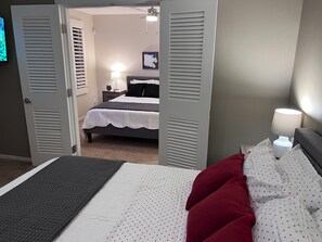Quarto de hotel com uma cama, mesa de cabeceira, abajur e porta que dá para outro cômodo.
