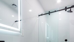 Ein modernes Badezimmer mit einer Glaskabine zur Dusche, einem weißen Waschbecken und einer Toilette.
