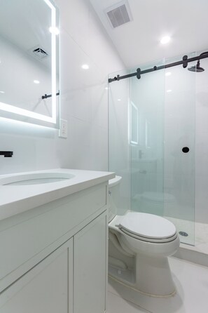 Ein modernes Badezimmer mit einer Glaskabine zur Dusche, einem weißen Waschbecken und einer Toilette.