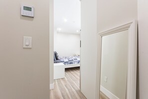 Ein Schlafzimmer mit einem Bett, einem Nachttisch, einem an der Wand montierten Thermostat und einer Tür.