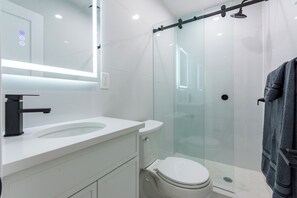 Ein modernes Badezimmer mit einer Duschkabine aus Glas, einem weißen Waschbecken und einem Spiegel mit integrierter Beleuchtung.
