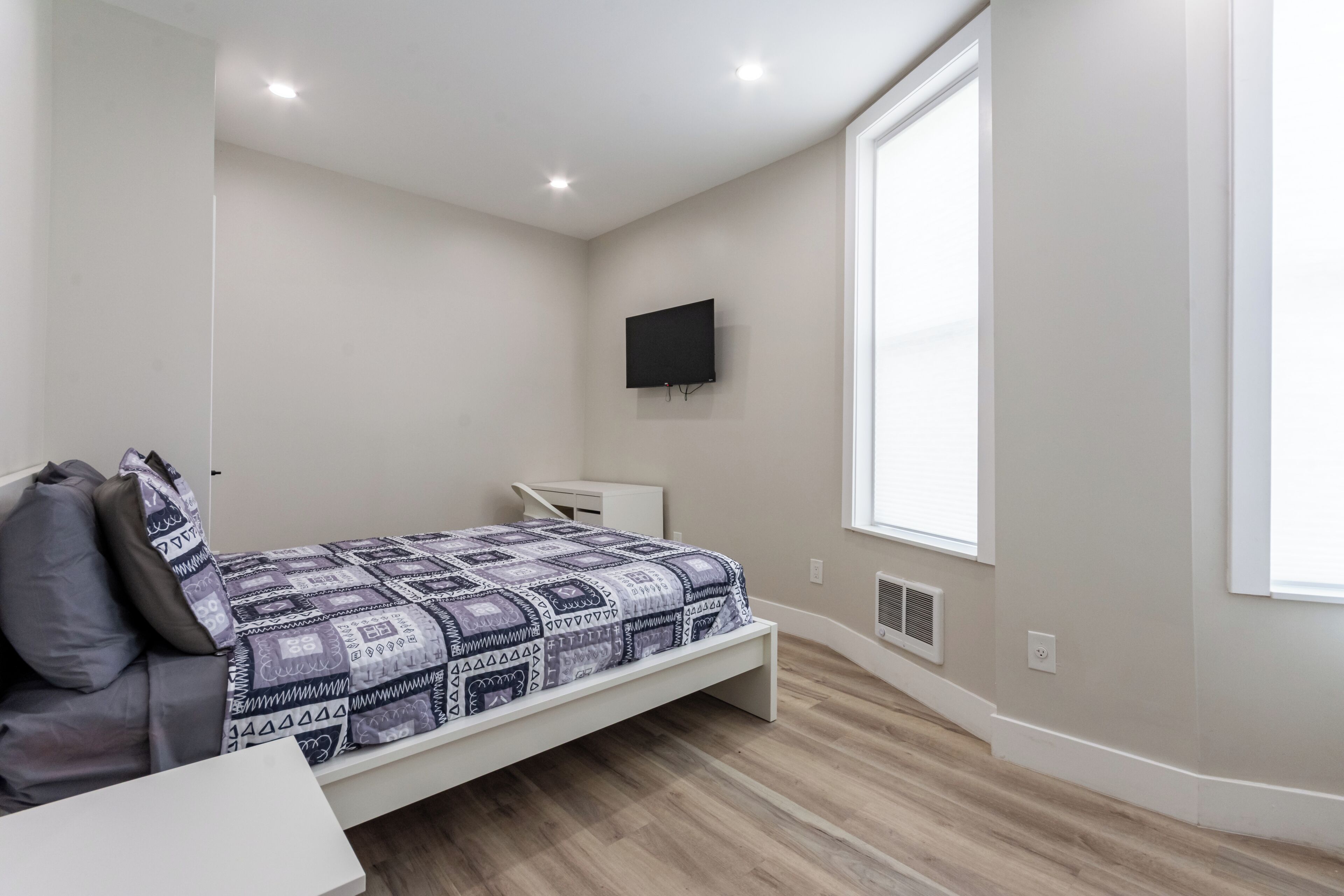 A bedroom with a bed, a desk, a TV, and a window.