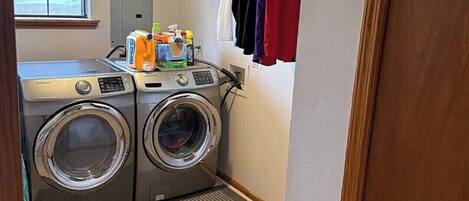 A laundry area with a front-loading washer and dryer, a window, and a door leading to another room.