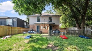 A residential backyard with a house, a fenced area, and outdoor seating. - Walk to AT&T Stadium | Modern 2BR, Free Parking (Arlington)
