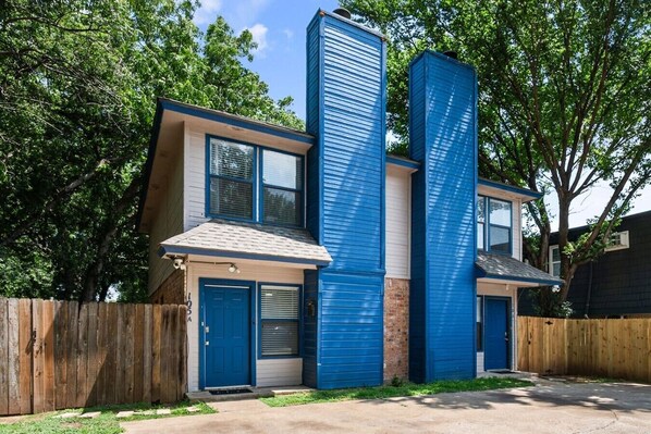 Un edificio residencial de dos pisos con fachada azul, una puerta principal y un portón de garaje.