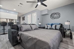 Ein modernes Schlafzimmer mit einem großen Bett, einem Deckenventilator und einem Essbereich mit Barhocker.