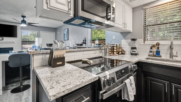 A modern kitchen with a central island, stainless steel appliances, and a window with blinds. - Walk to AT&T Stadium | Modern 2BR, Free Parking (Arlington)