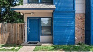 A two-story building with a blue door and a garage door. - Walk to AT&T Stadium | Modern 2BR, Free Parking (Arlington)