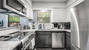 A compact kitchen with a built-in oven, a dishwasher, and a stainless steel refrigerator. - Walk to AT&T Stadium | Modern 2BR, Free Parking (Arlington)