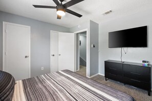 A bedroom with a bed, a dresser, a television, and a ceiling fan. - Game Day Modern 2BR | Steps to AT&T & Globe Life (Arlington)