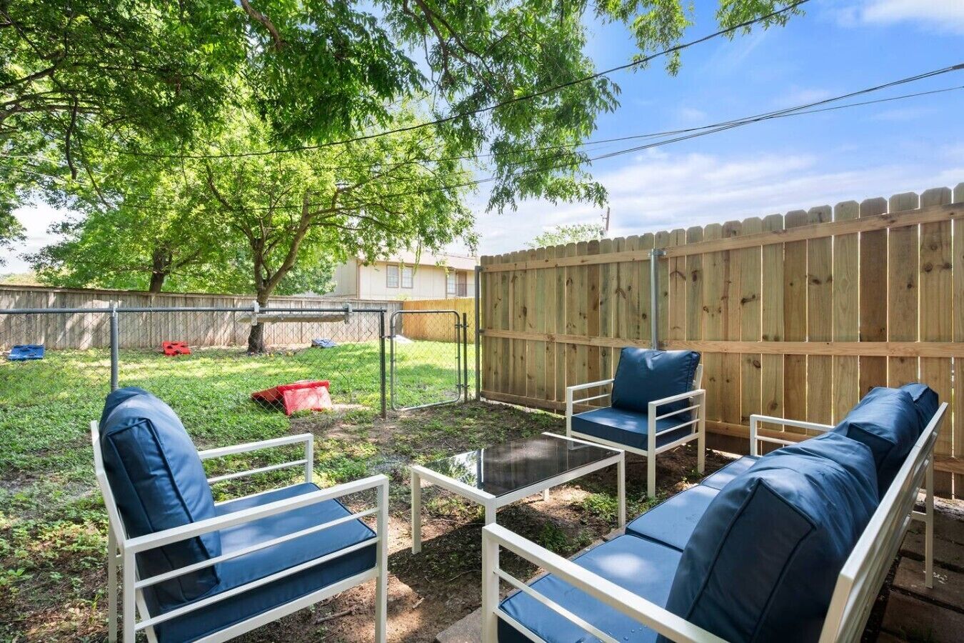 A backyard with a wooden fence, a tree, and outdoor furniture including a sofa and chairs.