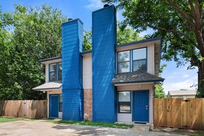 A two-story residential building with a blue exterior, a brick section, and a wooden fence in the background. - Game Day Modern 2BR | Steps to AT&T & Globe Life (Arlington)