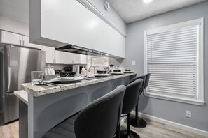 A modern kitchen with a central island, bar stools, and a built-in oven. - Game Day Modern 2BR | Steps to AT&T & Globe Life (Arlington)