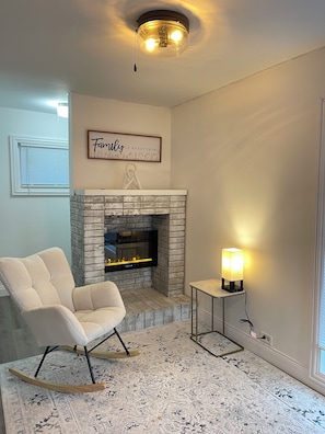Ein Wohnzimmer mit Kamin, einem Schaukelstuhl und einem an der Wand befestigten Fernseher.