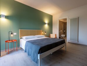 Een moderne slaapkamer met een bed, nachtkastjes, een radiator en een badkamer zichtbaar door een open deur.