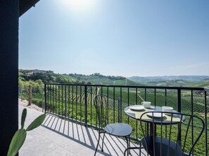 Een balkon met een tafel en stoelen, uitkijkend op een wijngaard.