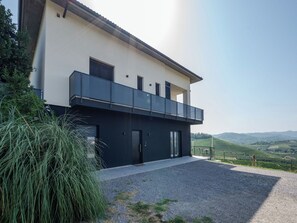 Een modern huis met twee verdiepingen, een balkon, een oprit met grind en uitzicht op het landschap.