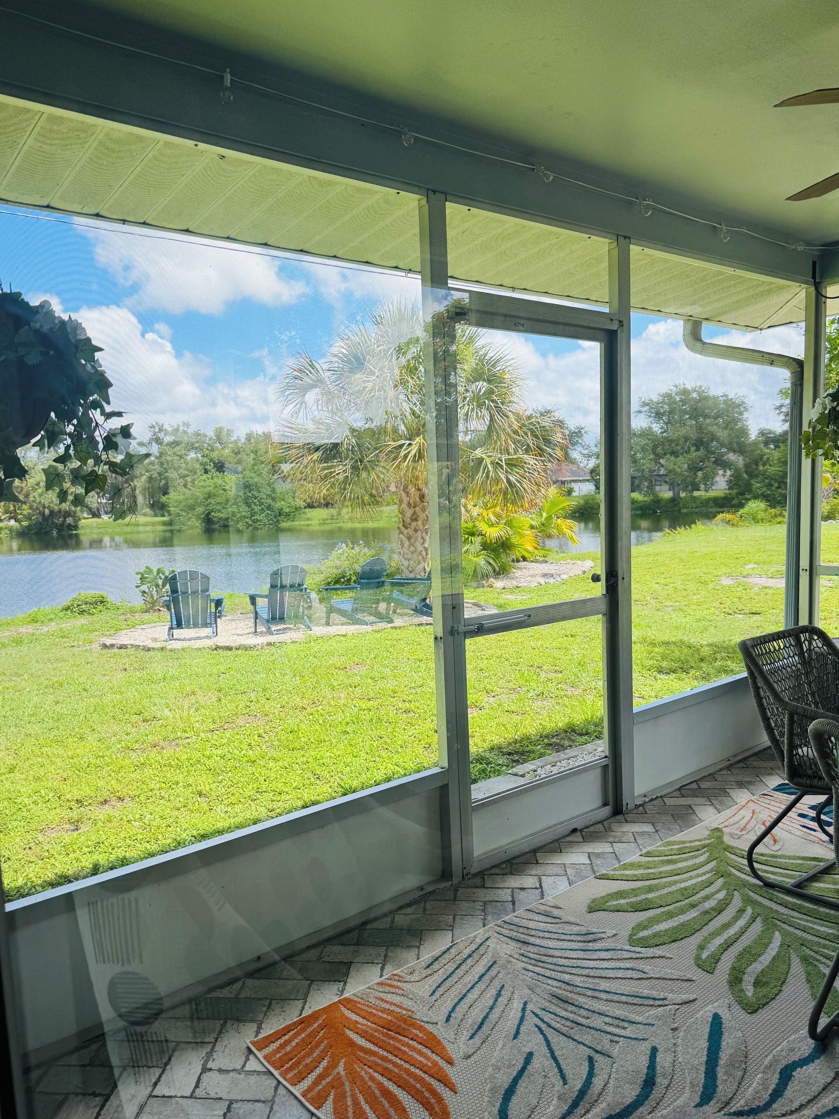 A covered patio with a view of a lake, chairs, and a patterned rug.