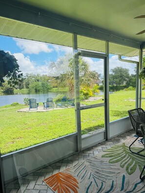 A covered patio with a view of a lake, chairs, and a patterned rug. - Stylish Lakefront Retreat, Pet Friendly, Flexible King/Twin Setup, Mins to Beach (Venice)