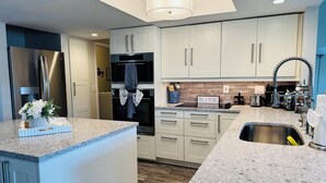 A modern kitchen with white cabinets, a stainless steel refrigerator, a built-in oven, and a granite countertop. - Stylish Lakefront Retreat, Pet Friendly, Flexible King/Twin Setup, Mins to Beach (Venice)