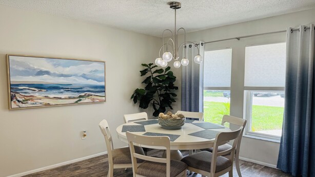 A dining area with a round table, white chairs, a potted plant, and a painting on the wall. - Stylish Lakefront Retreat, Pet Friendly, Flexible King/Twin Setup, Mins to Beach (Venice)
