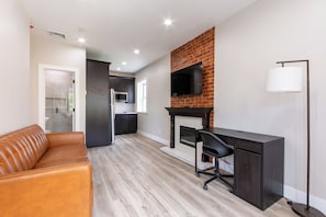 Un salon moderne avec un canapé en cuir, une cheminée, un téléviseur fixé au mur en briques et un bureau avec une chaise.