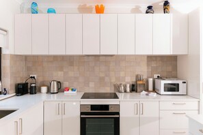 Une cuisine moderne avec des meubles blancs, un four encastré, un four à micro-ondes et divers appareils de cuisine.