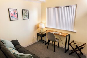 A compact living space with a desk, chair, and a couch. - A comfortable apartment with a charming view over Adelaide’s southern parklands. (Adelaide)