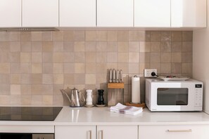 A kitchen with white cabinets, a microwave, a kettle, and a spice rack. - A comfortable apartment with a charming view over Adelaide’s southern parklands. (Adelaide)