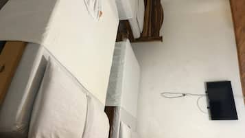 Una habitación con dos camas, un cabecero de madera, un objeto negro pequeño en la pared y una pared blanca.