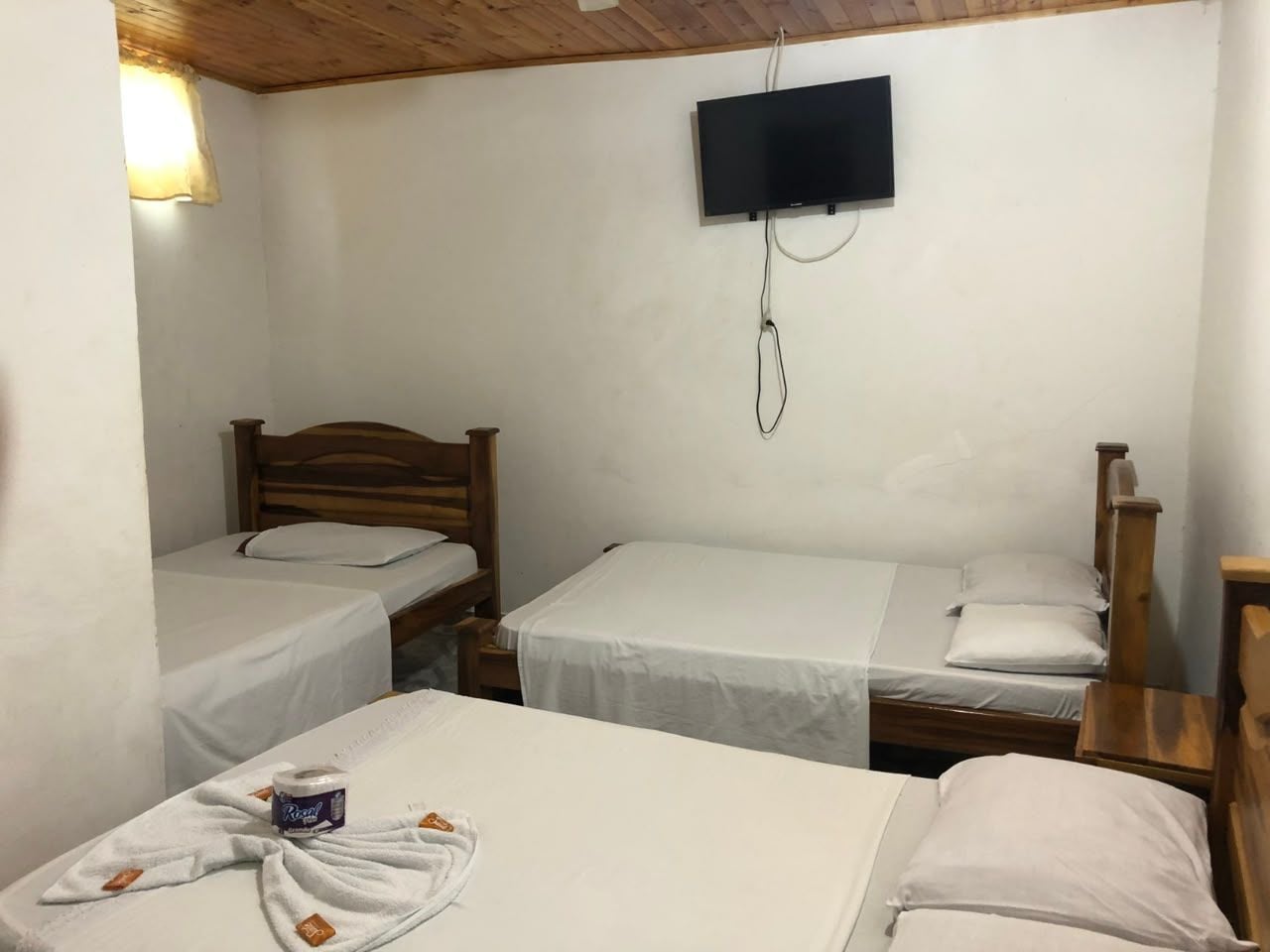 Una habitación con tres camas de madera, un televisor fijado a la pared y una lámpara.