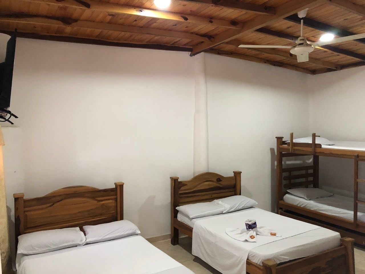 Une chambre avec deux lits simples et un lit superposé, des têtes de lit en bois, du linge de lit blanc et un ventilateur de plafond.