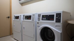 A laundry facility with three stacked washers and dryers, control panels, and a ventilation duct above. - Ski-In King Executive Resort Suite w/ Mtn Views, Pool & Garage! (Mammoth Lakes)